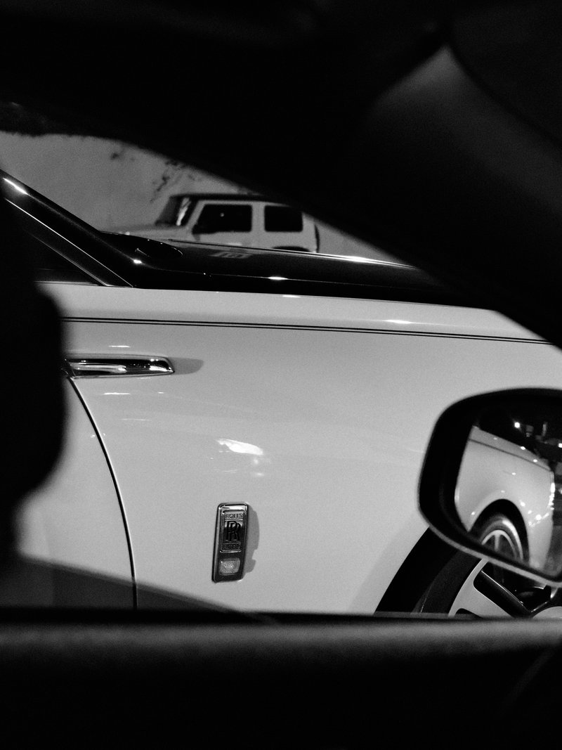 Close-up of a white luxury car seen through a side mirror in black and white.