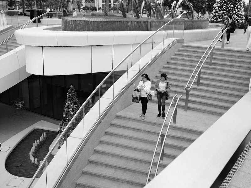Two women walking down a modern staircase in a public space with greenery and festive decorations.