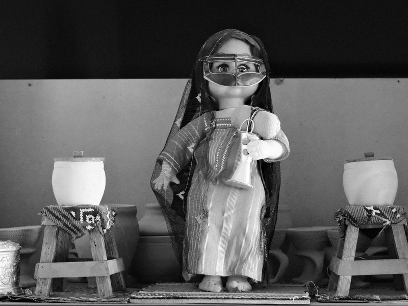 A traditional doll dressed in a long dress, holding a small object, flanked by two candles.