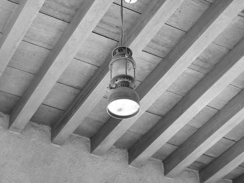 A vintage lantern hanging from wooden beams in a rustic interior setting.