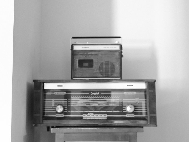 Two vintage radios stacked on a shelf against a plain wall.