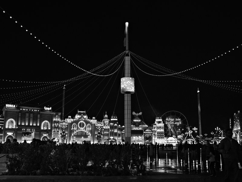 Nighttime view of a brightly lit amusement park with decorative lights and a clock tower.