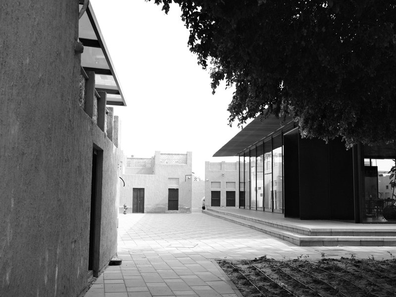 A modern building beside a traditional structure, with a clear sky and trees casting shadows.