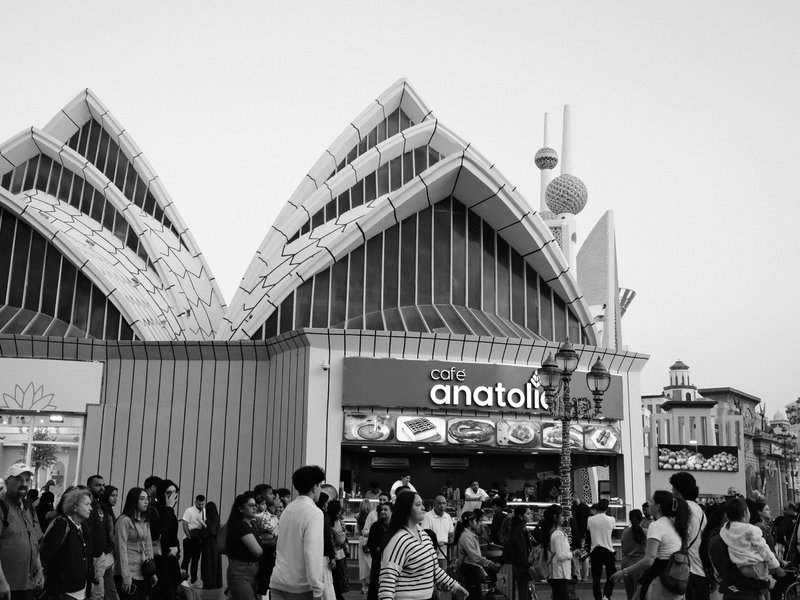 Crowd of people walking in front of a modern building with unique architecture in black and white.