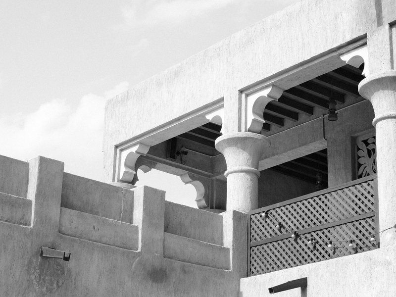 Architectural detail of a building with arches and a balcony against a cloudy sky.