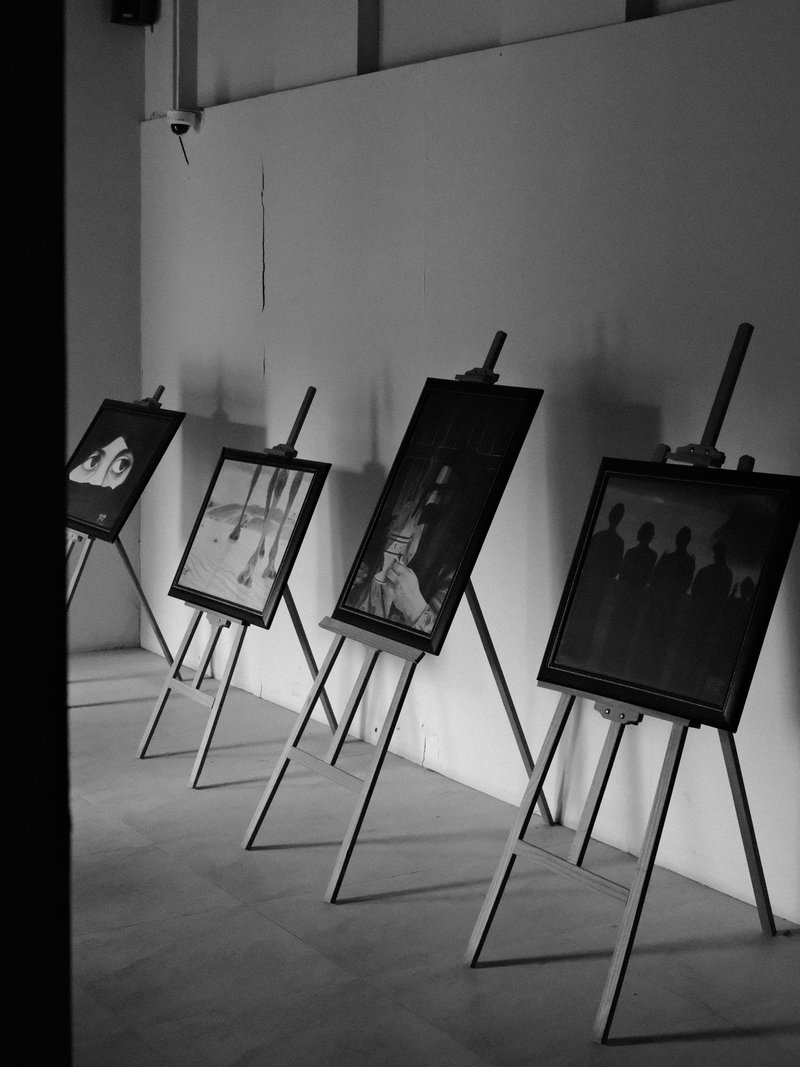 A gallery space with several black and white paintings displayed on easels against a white wall.