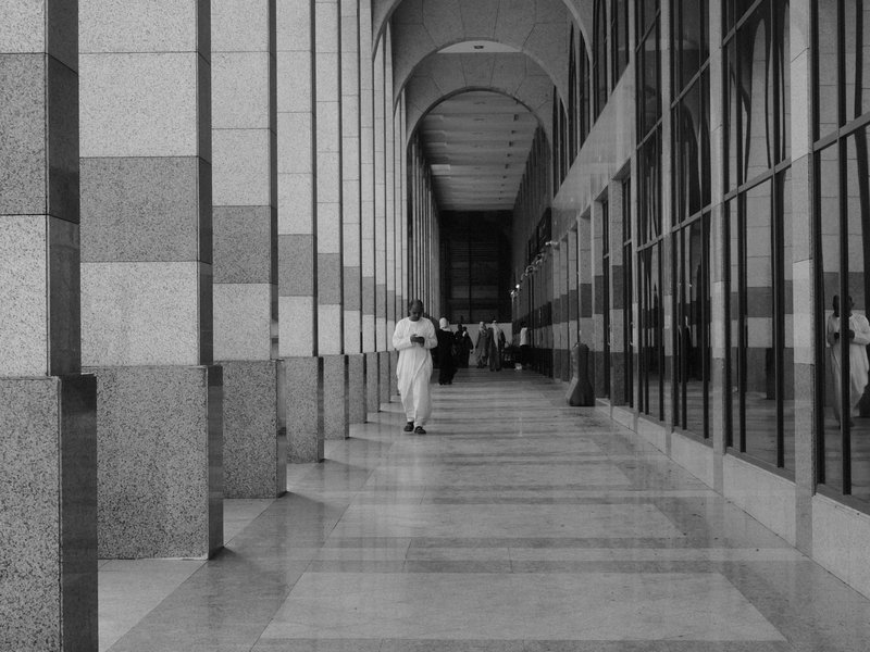 A long corridor with arches and reflective glass walls, featuring a person in white clothing walking.