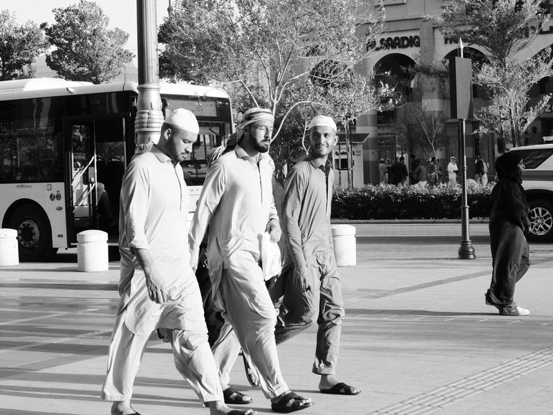 Three men walking together on a city street with a bus in the background.