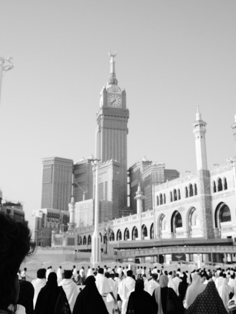 A crowd of people in traditional attire walking towards a large clock tower in a cityscape.