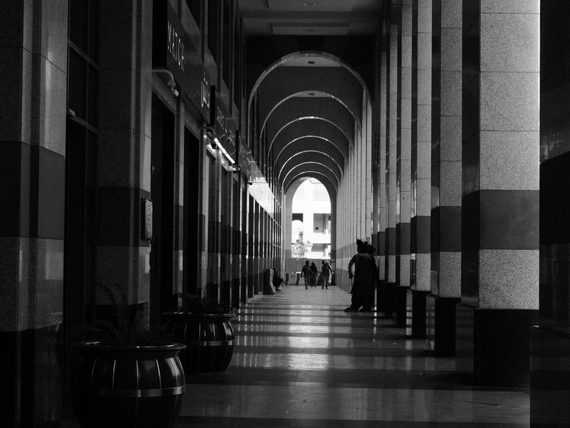 A long corridor with arches and striped columns, featuring people walking in the distance.