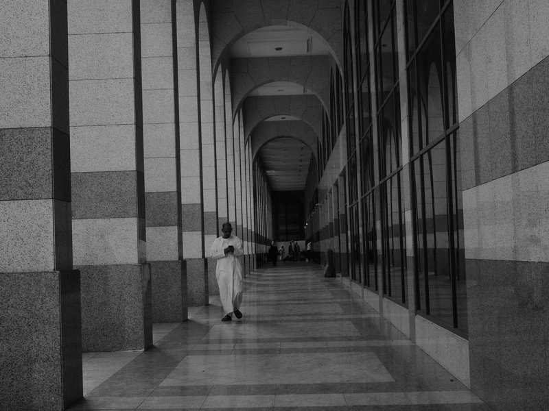 A person stands in a long corridor with arches and large glass windows, creating a dramatic perspective.