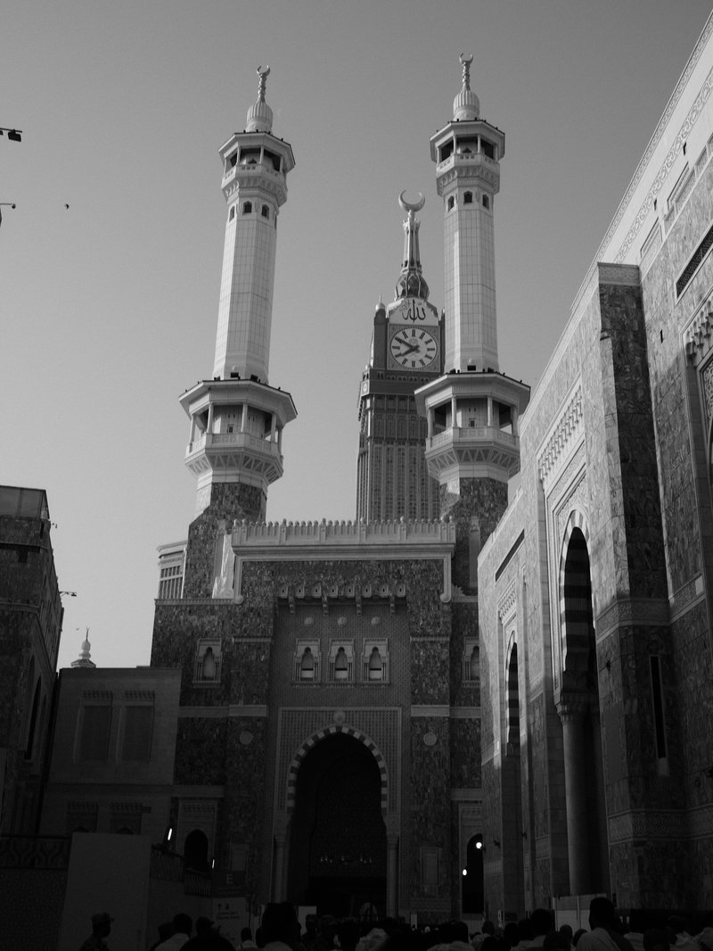 A historic mosque with tall minarets and a clock tower, set against a clear sky.