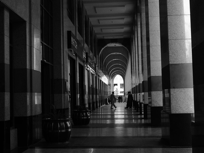 A person walking through a long, arched corridor with striped columns and soft light at the end.