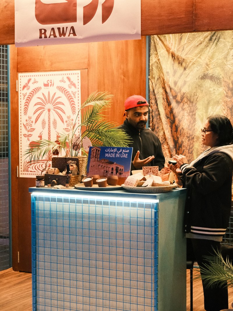 Two people at a market stall with decorative items and plants, illuminated by warm light.