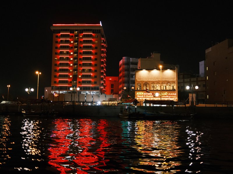 Night view of buildings with red lights reflecting on water.