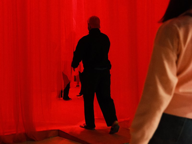 Silhouetted figures walking through a red fabric curtain, creating a striking contrast with the background.