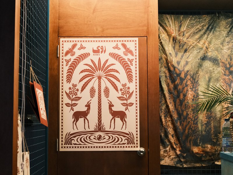 A decorative door featuring a palm tree and deer design, with a textured backdrop of fabric.