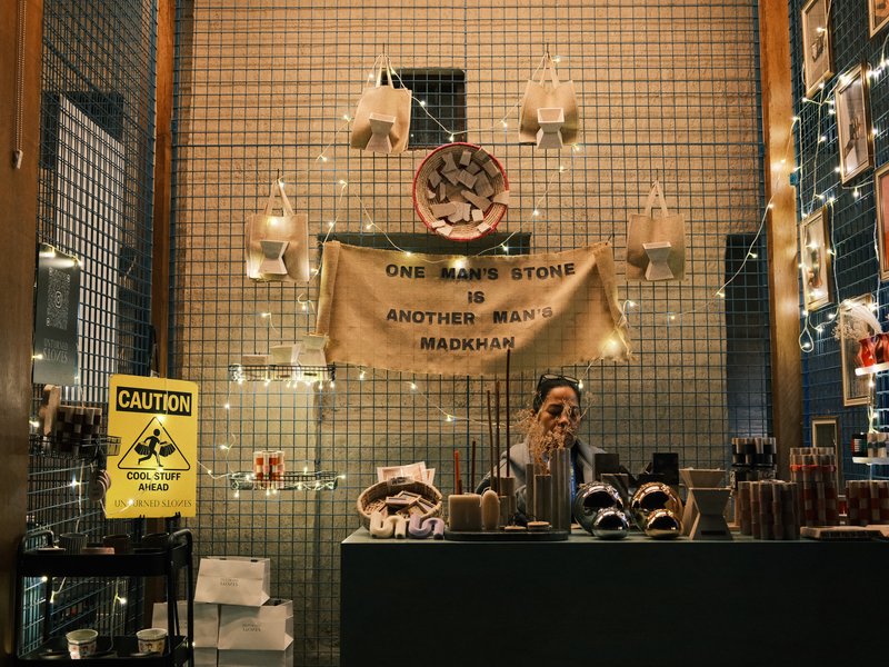 A cozy shop interior with a smiling vendor behind a counter, decorated with lights and a banner.