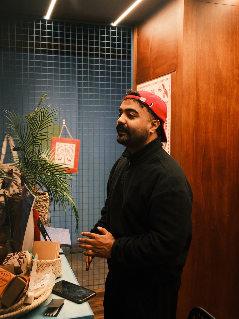 A man in a red cap stands in a cozy indoor setting with wooden walls and plants.
