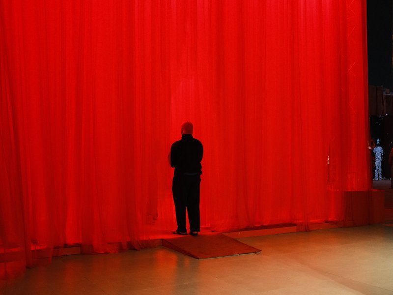 A silhouette of a person standing in front of a bright red curtain on a stage.