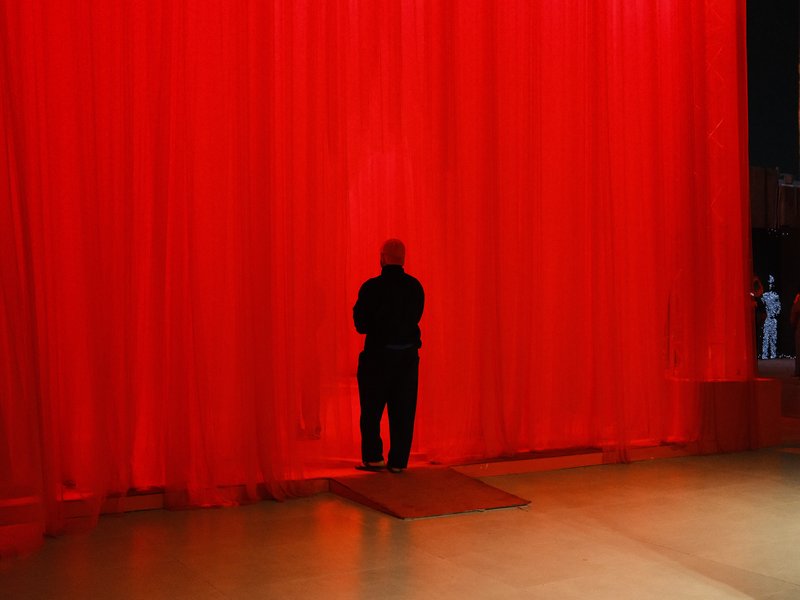 A silhouette of a person standing in front of a bright red curtain, creating a dramatic atmosphere.