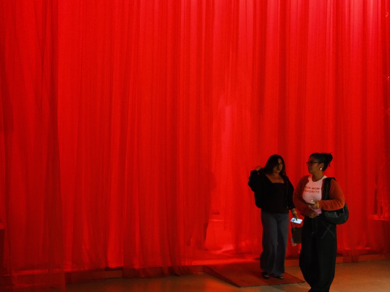 Two figures walking in front of a large red curtain, creating a striking contrast in the scene.
