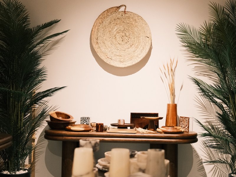 A wooden table adorned with decorative items, surrounded by green plants against a neutral wall.