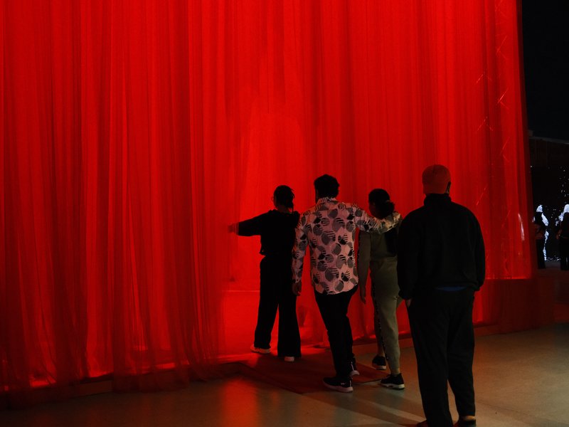 Four figures silhouetted against a vibrant red curtain, creating a dramatic and artistic scene.