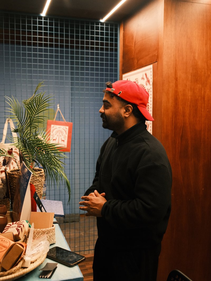 A man in a red cap stands beside a table filled with decorative items in a warmly lit indoor setting.