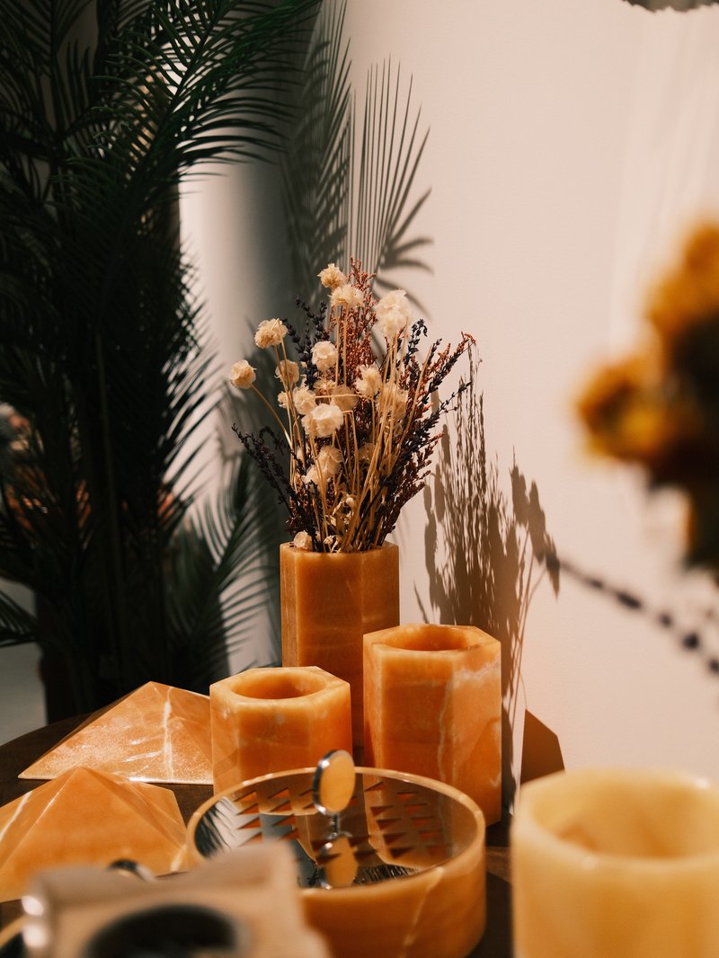 A still-life arrangement featuring yellow vases with dried flowers, surrounded by decorative items and shadows.