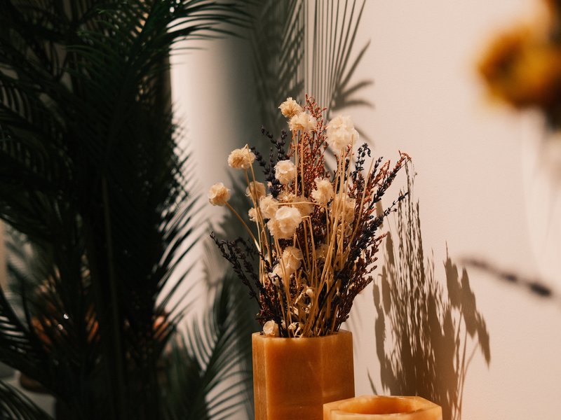A close-up of dried flowers in a vase with palm leaves in the background, creating soft shadows.