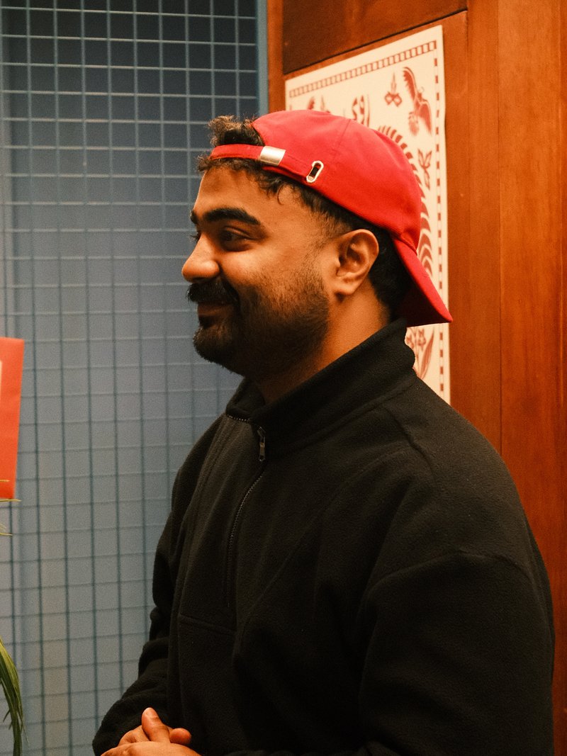A man wearing a red cap and black jacket stands in a room with blue tiled walls.