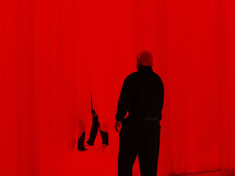 A silhouetted figure stands in front of a bright red curtain, holding a black and white object.