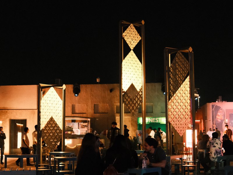 Night scene featuring illuminated decorative structures with people gathered around in an outdoor setting.