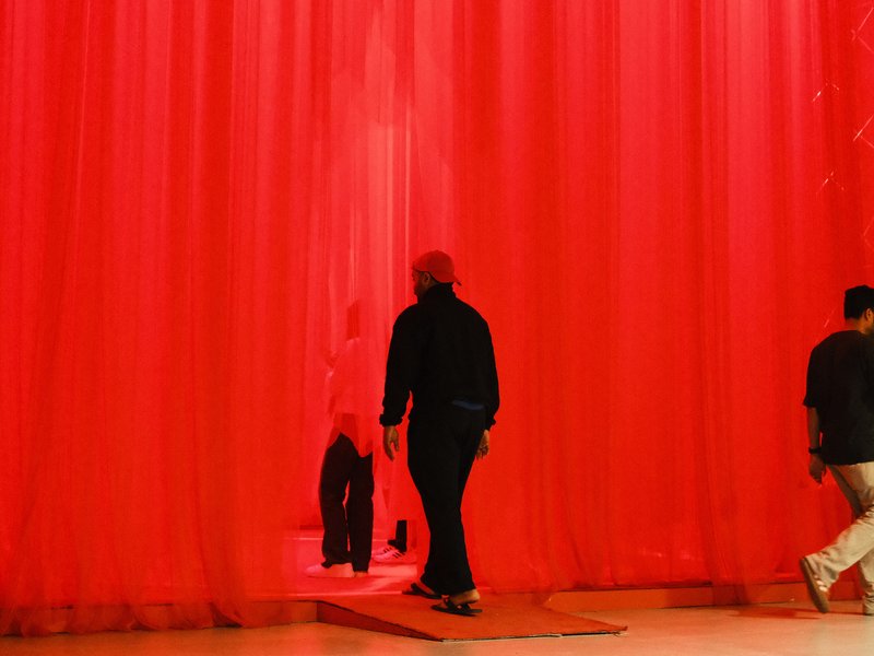 Two figures walking through a red curtain, creating a striking contrast with the vibrant background.