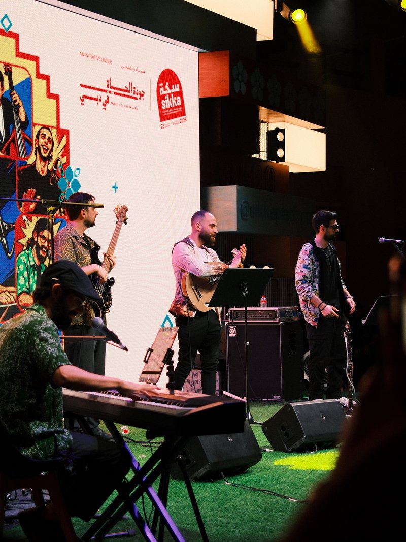 A live music performance with musicians on stage, colorful backdrop, and vibrant lighting.
