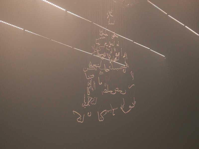 Abstract light patterns illuminating Arabic calligraphy on a dark background.
