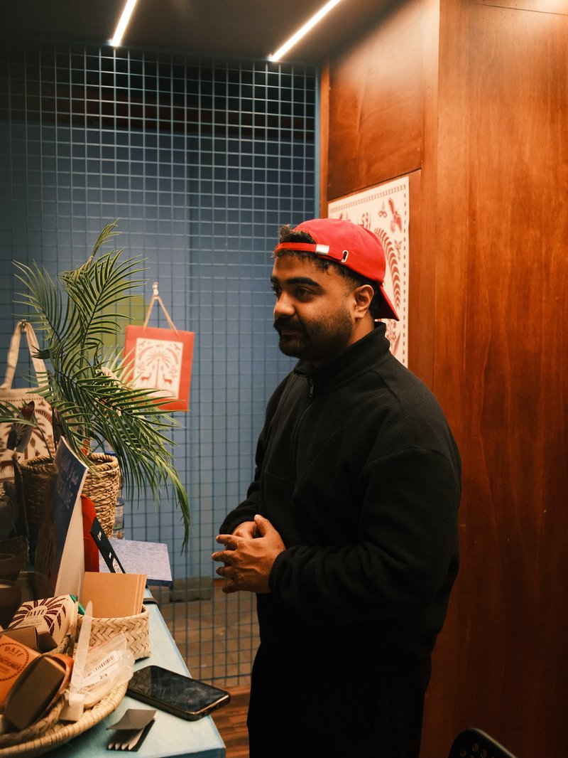 A man in a black jacket and red cap stands in a modern indoor space with wooden walls and plants.