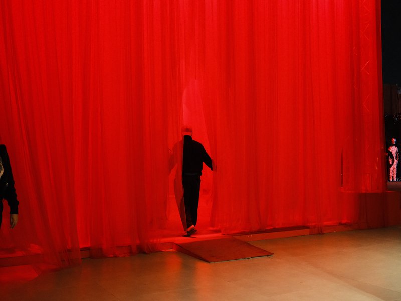 Silhouette of a person walking through a red curtain in a dimly lit space.