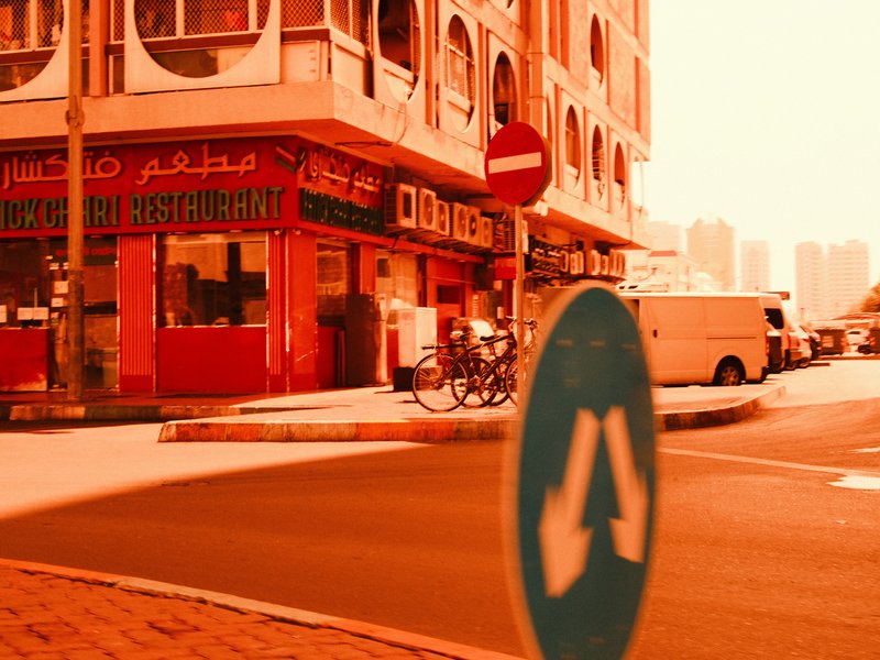 Street scene featuring a red building with signage, a bicycle, and a traffic sign indicating directions.
