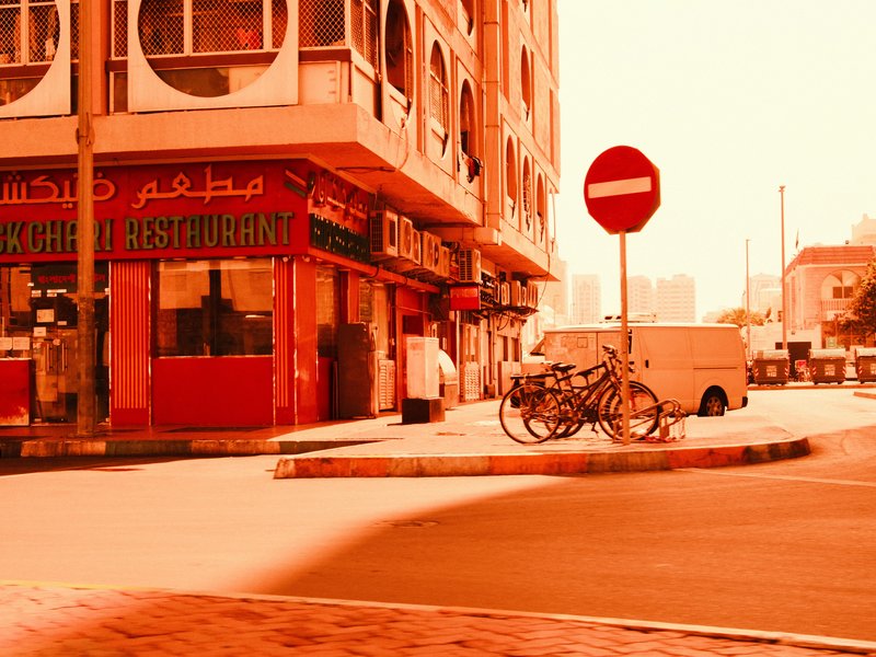 Urban street scene featuring a red-themed restaurant and parked bicycles under warm lighting.