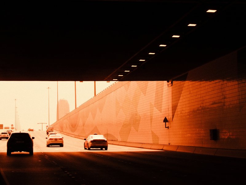 Cars driving through a tunnel with warm orange lighting and a textured wall in the background.