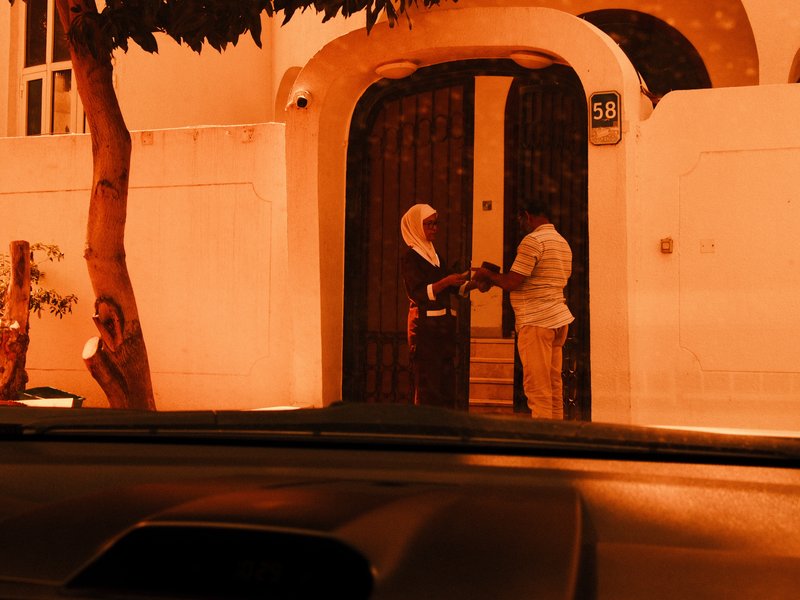 Two people interacting at a doorway, illuminated by warm orange light, with a tree nearby.