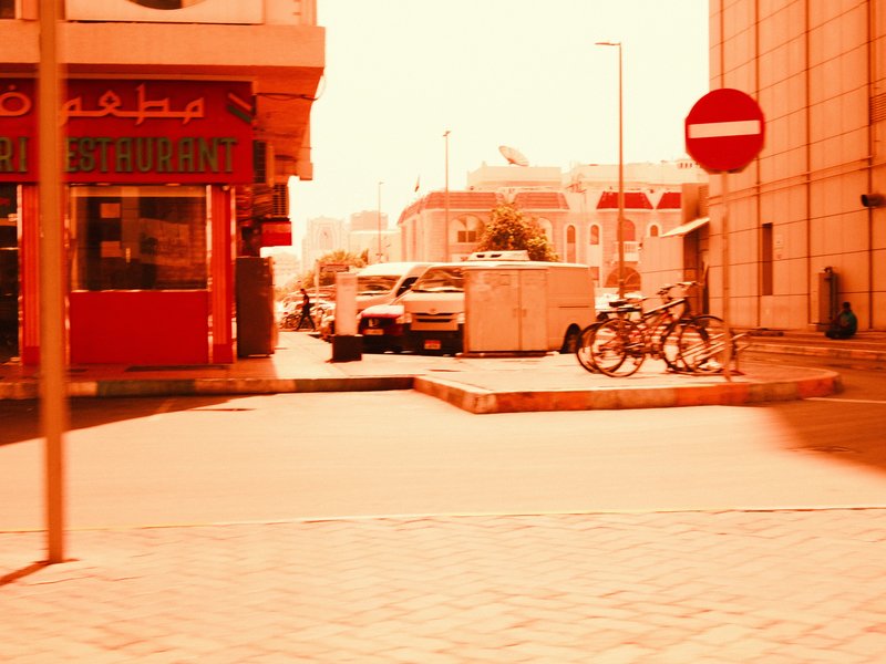 A street scene with a red storefront, parked cars, and a bicycle near a no-entry sign.