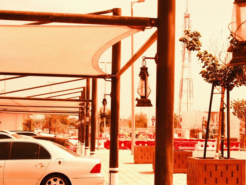A parking area with cars, wooden structures, and a vintage lantern under a warm orange hue.