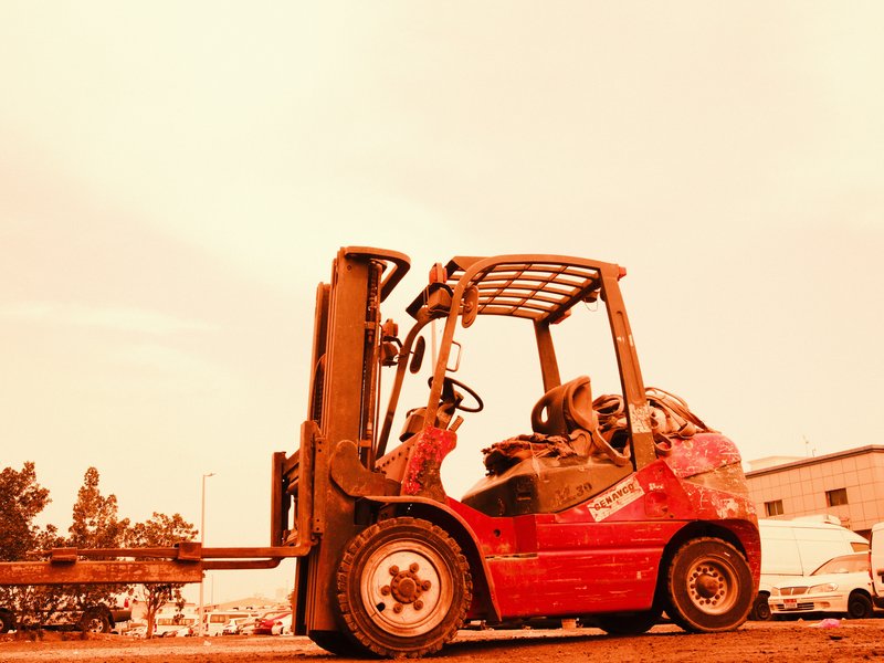 A red forklift parked in an industrial area under a bright orange sky.