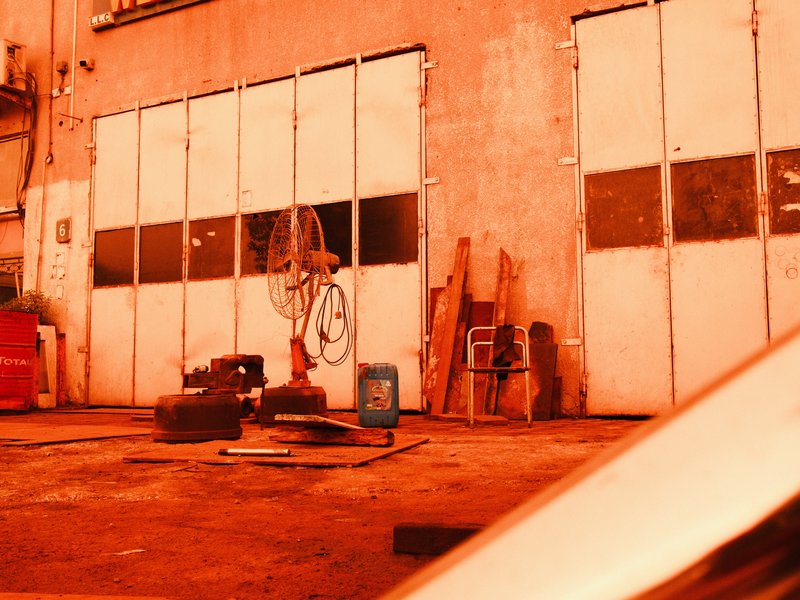 An industrial garage with large doors, tools, and scattered materials in an orange hue.