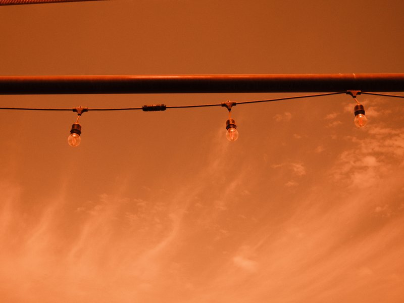 String lights hanging against a warm orange sky with wispy clouds.