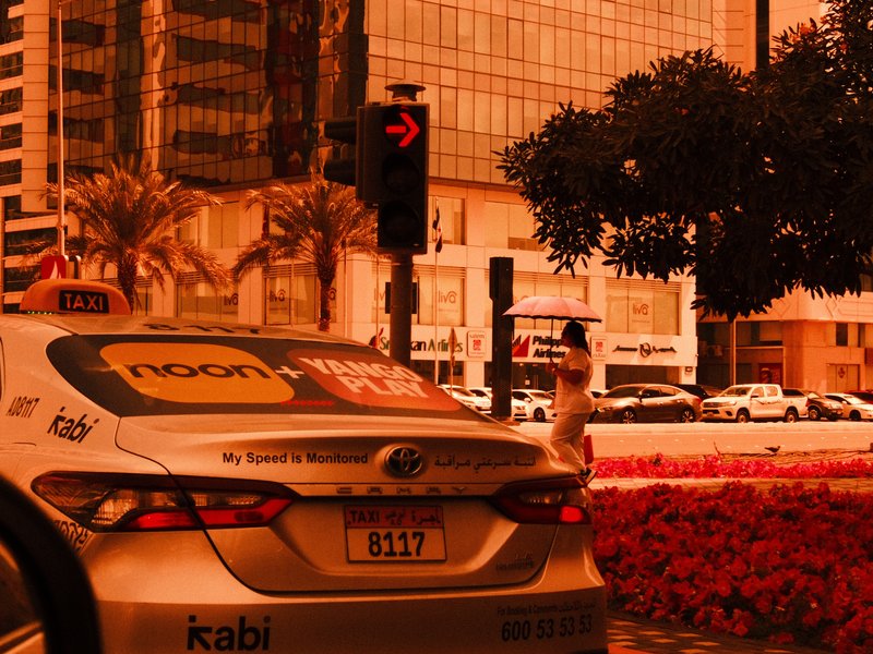 A taxi parked at a traffic light in an urban setting with palm trees and buildings in the background.