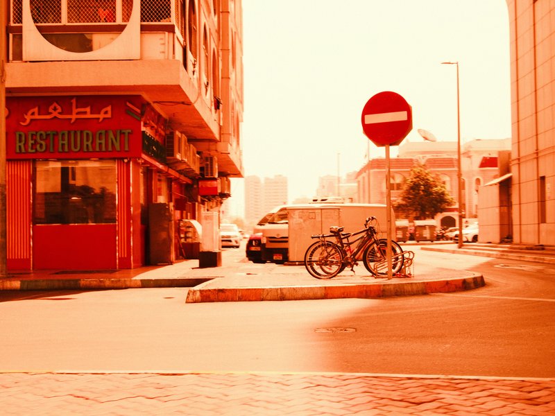 A street scene featuring a restaurant, parked bicycles, and a no-entry sign under an orange hue.